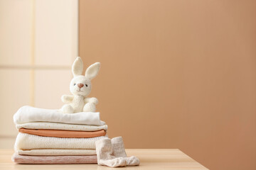 Stack of baby clothes, socks and toy bunny on table against color wall