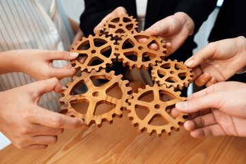 Closeup hand holding wooden gear by businesspeople wearing suit for harmony synergy in office...