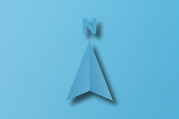 Light blue paper cut shape north arrow set on light blue paper background.