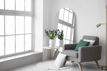 Interior of living room with mirror, armchair and tulips in vase
