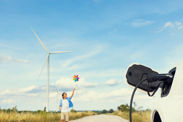 Progressive young asian boy playing with wind pinwheel toy in the wind turbine farm, green field...