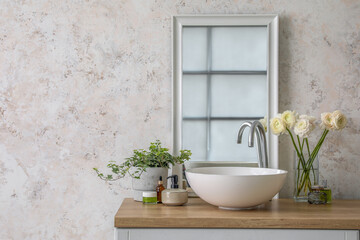 Fototapeta na wymiar Vase with flowers, sink, mirror and bath accessories on counter in bathroom