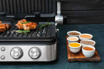 Modern electric grill with delicious steaks and spices on grey grunge table