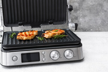Modern electric grill with delicious steaks on white grunge table
