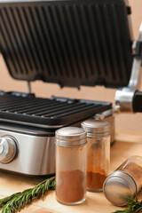 Modern electric grill with open lid, spices and rosemary on wooden table, closeup