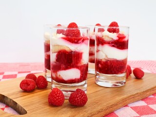4 glasses filled with tiramisu and raspberry coulis. Tasty dessert served on a wooden board and decorated with fresh raspberries.