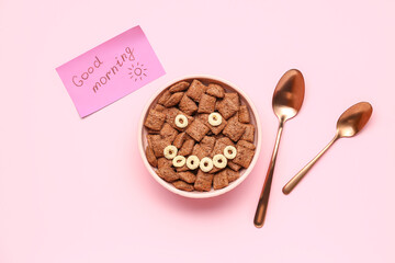 Bowl of tasty corn pillows, spoons and paper with text GOOD MORNING on pink background