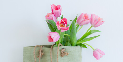 Pink tulips bouquet in green shopping bag on white background copy space banner