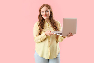 Beautiful redhead woman with laptop on pink background