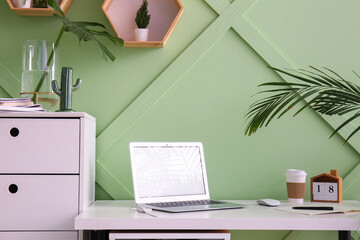 Workplace with laptop and cup of coffee near green wall in office