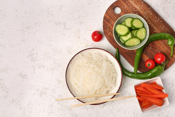 Composition with bowl of tasty rice noodles, chopsticks and vegetables on white grunge table
