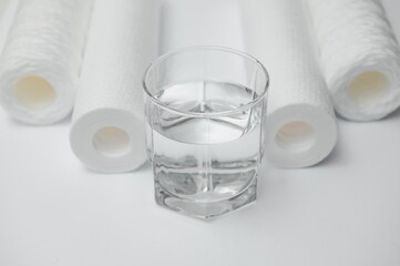 Water filters. Carbon cartridges and a glass on a white background. Household filtration system
