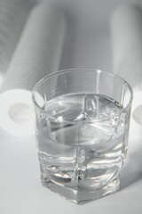 A glass of drink water and filter cartridges at white background