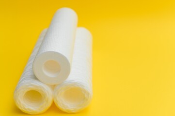 Water filters. Carbon cartridges and a glass on a yellow background. Household filtration system