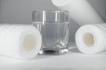 A glass of drink water and filter cartridges at white background