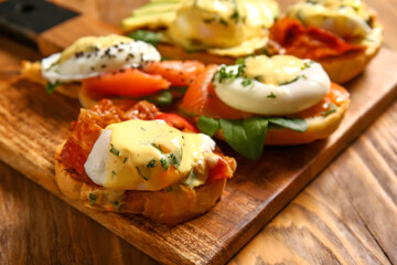 Board with different eggs Benedict on wooden table, closeup