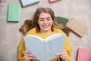 Young woman reading book on floor at home, top view