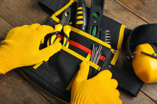Male hands in gloves taking tools from belt on wooden table
