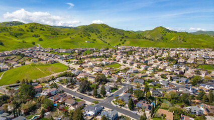 Drone photos over the city of Antioch, California on a beautiful blue day with green hills, homes and streets.