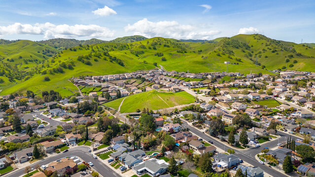 Drone photos over the city of Antioch, California on a beautiful blue day with green hills, homes and streets.