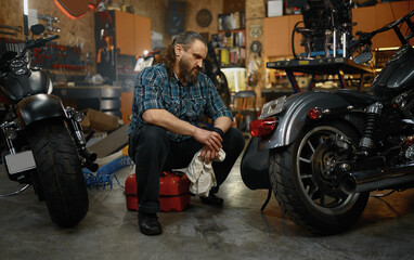 Obraz na płótnie Canvas Bearded mature man biker cleaning motorcycle in garage workstation