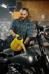 Fototapeta na wymiar Man biker refueling motorcycle in garage after service repair work