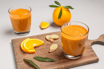 Board with glasses of healthy orange smoothie and ingredients on grey background