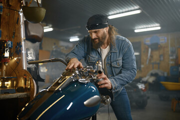 Fototapeta na wymiar Mature male biker examining his new motorbike standing with garage