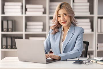 Asian Businesswoman Using laptop computer and working at office with calculator document on desk, doing planning analyzing the financial report, business plan investment, finance analysis concept.
