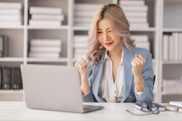 Excited happy woman looking at the laptop computer screen, celebrating an online win, overjoyed young asian female screaming with joy, isolated over a white blur background
