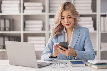 Asian women hold smartphone and use pc at the workplace. Project stats financial data sales charts on laptop and cellphone
