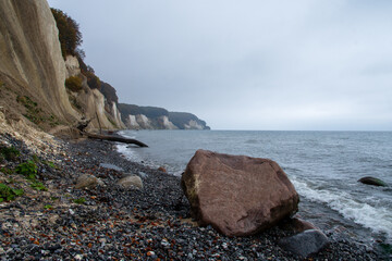 low angle view on the Rügen Chalk cliffs with overcast sky and a big stone lying on the shore in the surf