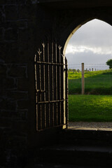 an open fenced gate in an irish monastery ruin looking out of the dark room onto a green pasture