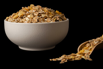 close-up of a white bowl of muesli with wooden spoon with flakes isolated on black background and copy space