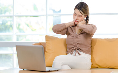 Asian upset suffered frowning face young female housewife sitting working with laptop on sofa couch in living room at home holding hands on neck suffering from shoulder ache from office syndrome