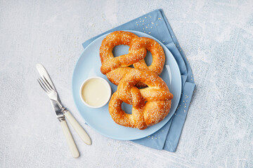 Plate with tasty pretzels and condensed milk on light background