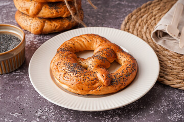 Plate with tasty pretzel and poppy seeds on grunge background