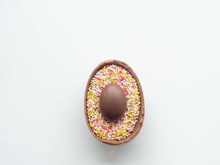 Sweet Easter concept. Chocolate easter egg with sweet sprinkles on white background with copy space. Design for a greeting card for the Easter holiday. Flat lay. Preparation for holiday.