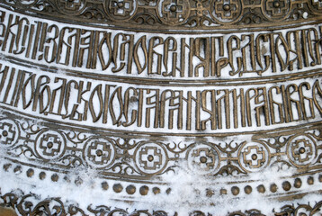 detail of inscription in Cyrillic on a giant gold colored church bell with snow 
