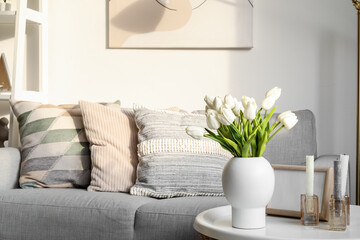 Vase with artificial tulips and candles on table in living room