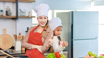 Asian young cheerful female mother and little cute girl daughter wearing white tall cook hat and...