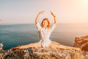 Happy smiling teen girl balerina performs stretching exercises splits on the beach during a beautiful sunset, enjoying a sunny summer day. © panophotograph