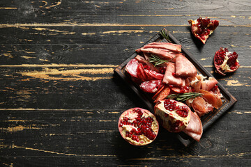Board with assortment of tasty deli meats on dark wooden background