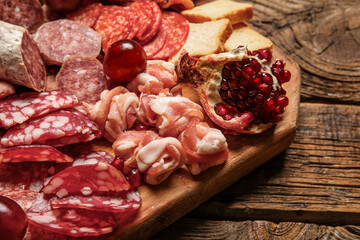 Board with assortment of tasty deli meats on wooden background, closeup