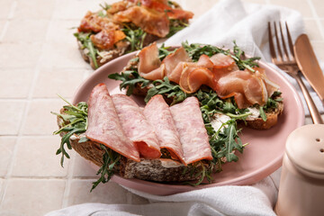 Tasty bacon, jamon and ham bruschettas with arugula on tile background