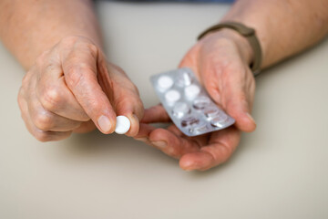 Senior woman with wrinkled old hands at the table holding one round medical tablet, painkiller or pill for treatment. Healthcare and medicine concept