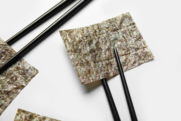 Chopsticks with nori sheets on white background, closeup