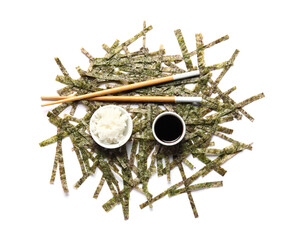Heap of cut nori sheets, rice, soy sauce and chopsticks on white background