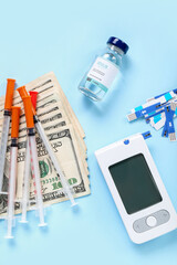 Insulin with glucometer, lancet pens, syringes and money on blue background. Expensive medicine concept