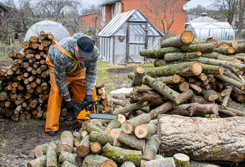 man in yellow rubber pants prepares firewood, sawing firewood, heating concept, energy crisis